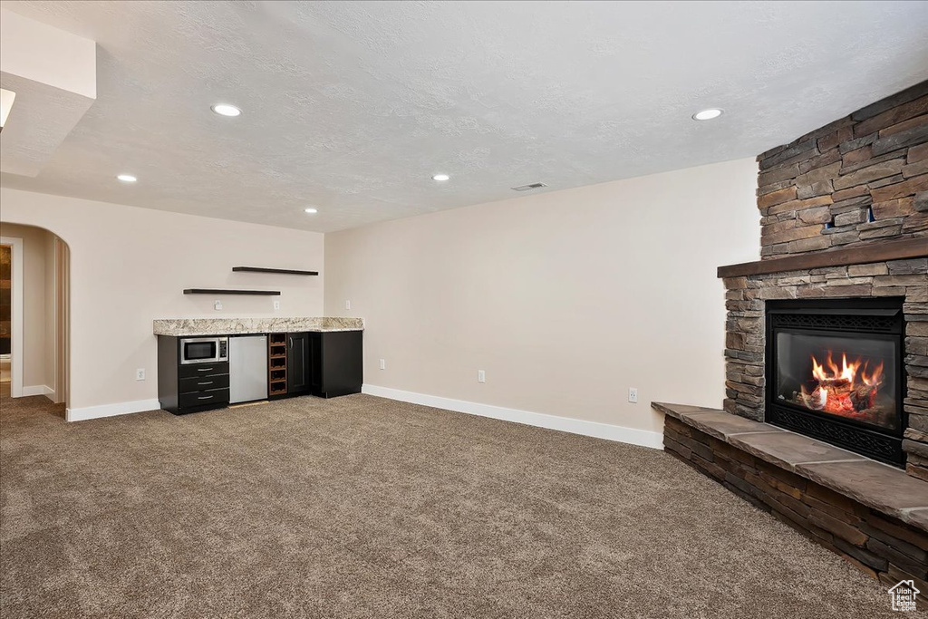 Unfurnished living room featuring baseboards, arched walkways, a stone fireplace, a textured ceiling, and carpet flooring