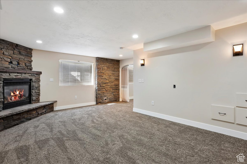 Unfurnished living room featuring baseboards, arched walkways, carpet flooring, and a stone fireplace