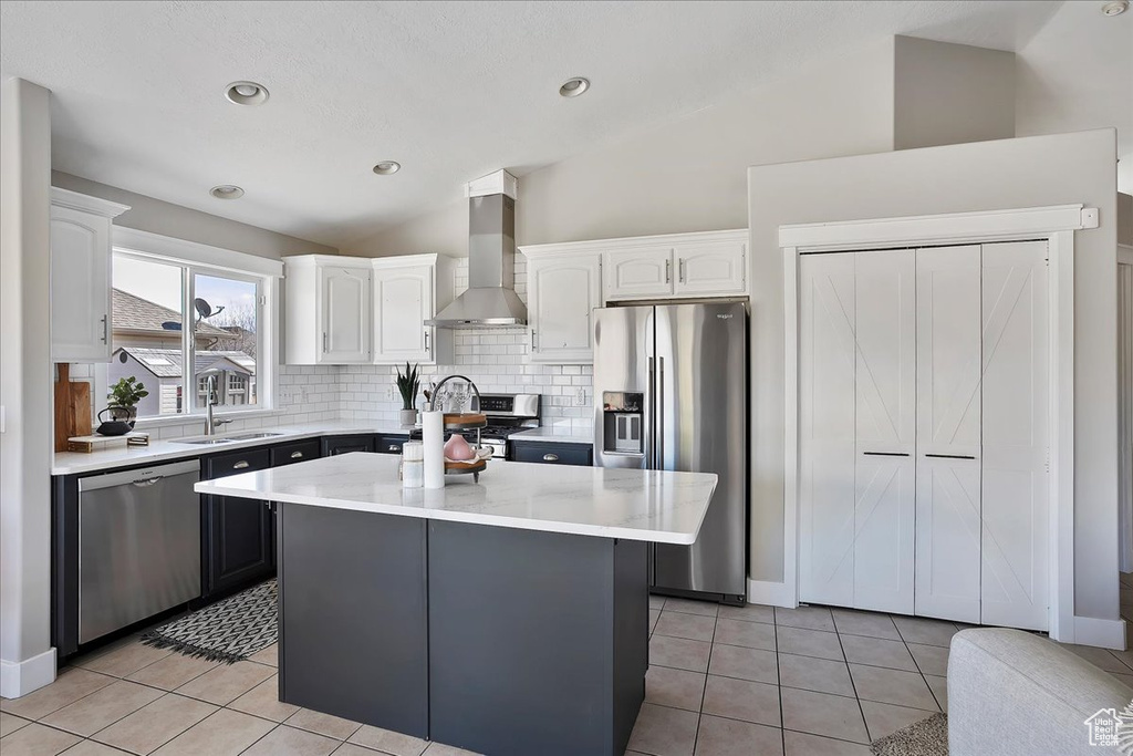 Kitchen featuring stainless steel appliances, lofted ceiling, white cabinetry, a sink, and wall chimney range hood