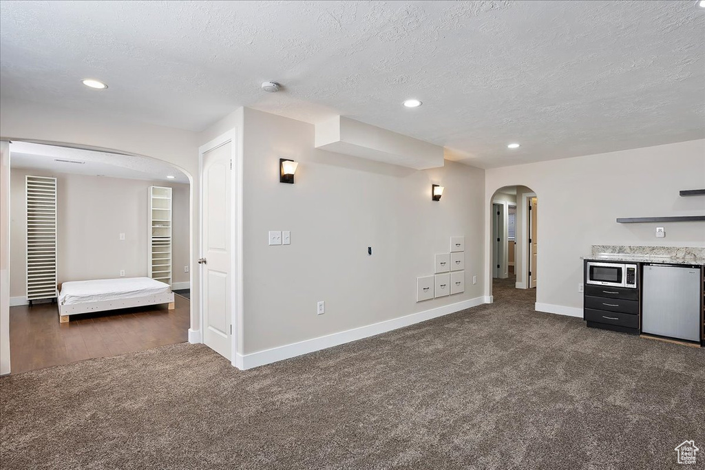 Unfurnished living room featuring arched walkways, recessed lighting, dark carpet, a textured ceiling, and baseboards