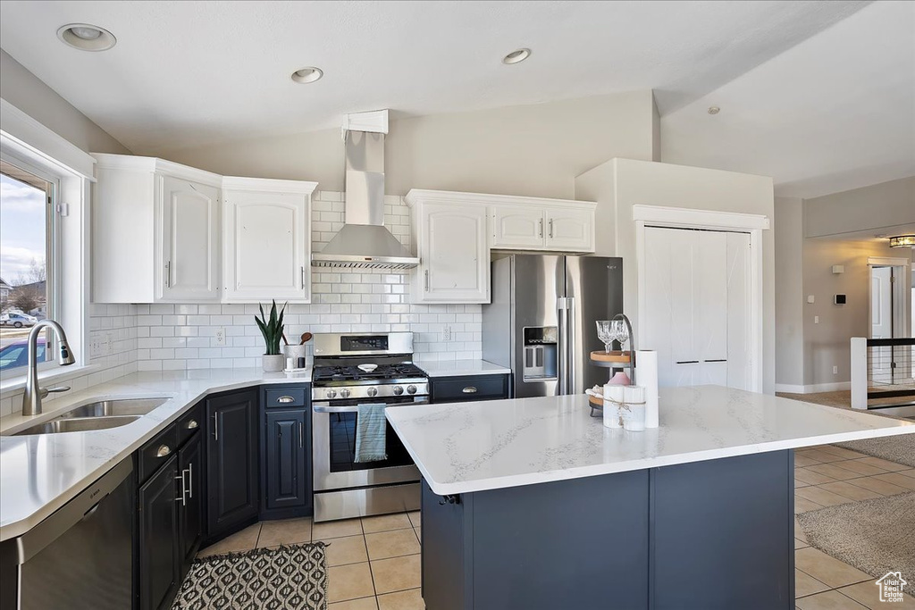 Kitchen featuring a sink, appliances with stainless steel finishes, vaulted ceiling, and wall chimney range hood