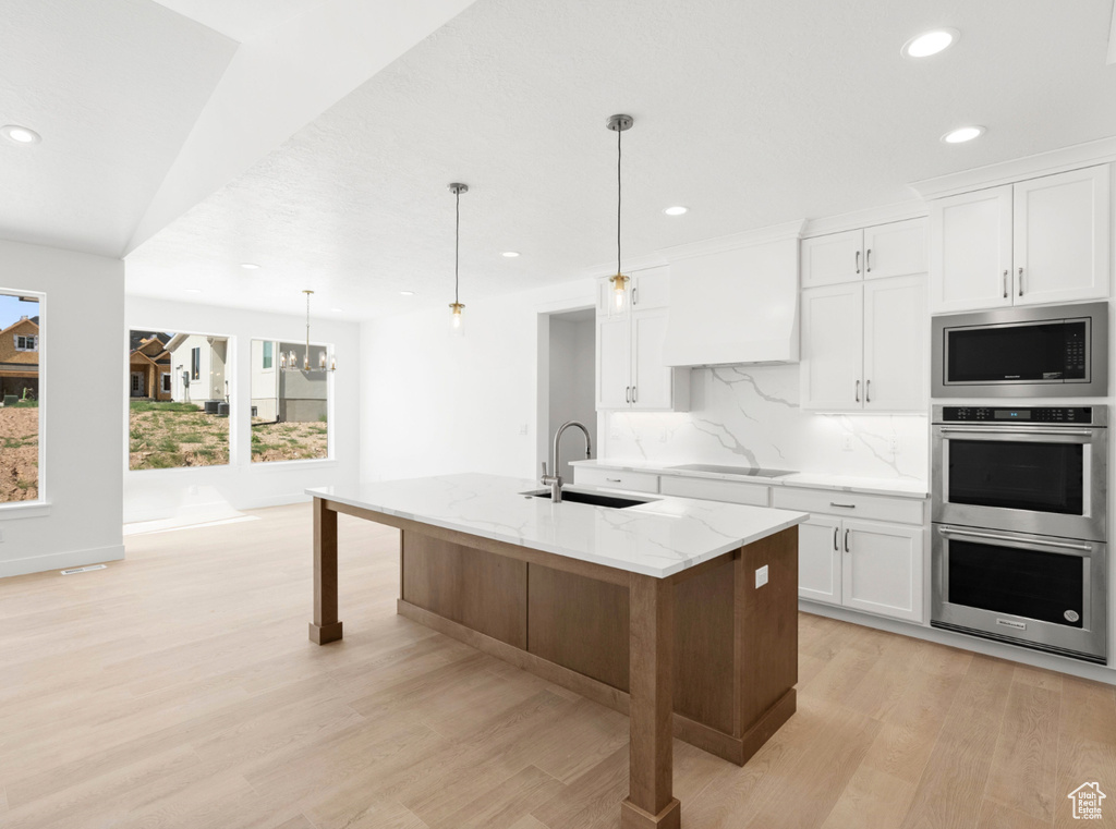 Kitchen featuring appliances with stainless steel finishes, light wood finished floors, recessed lighting, backsplash, and light stone countertops