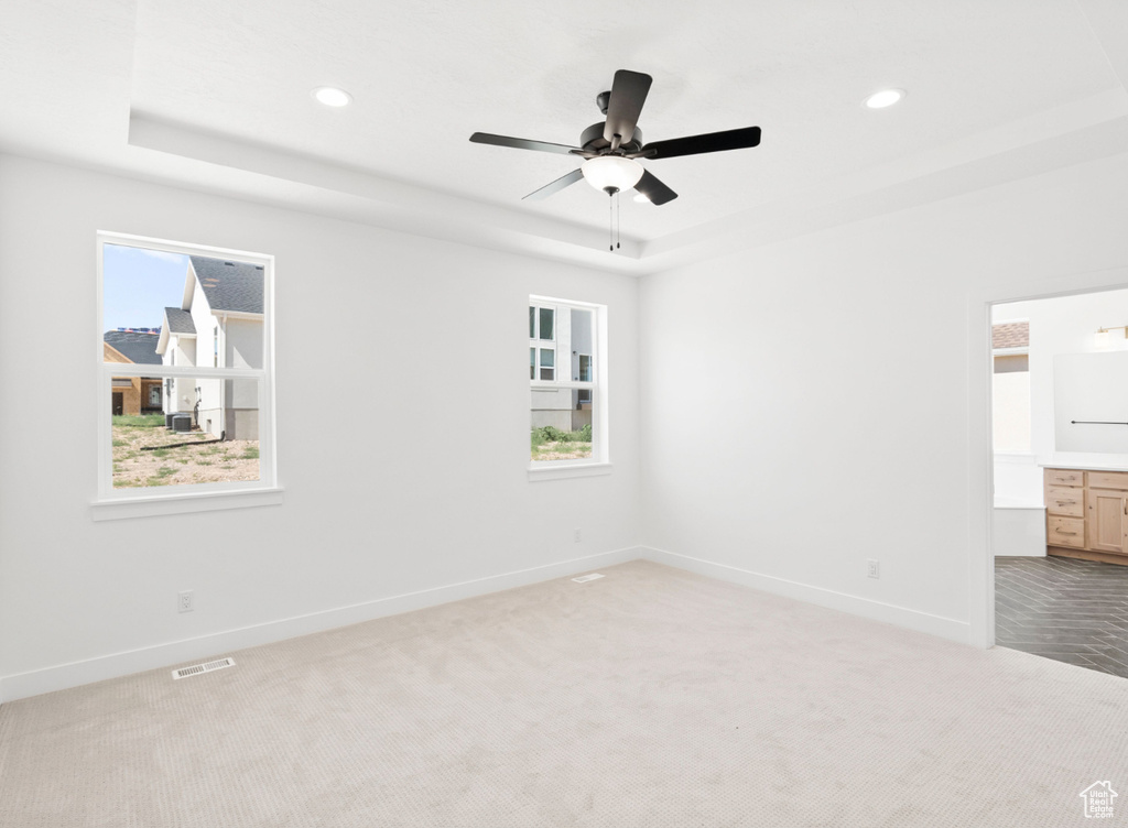 Unfurnished room featuring a raised ceiling, light colored carpet, a ceiling fan, and recessed lighting