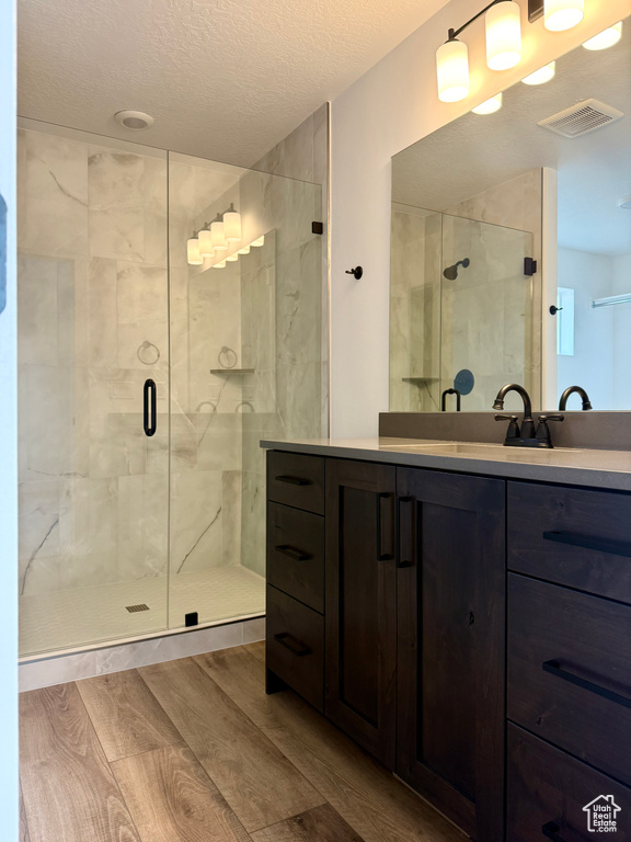 Full bath with a shower stall, visible vents, wood finished floors, and vanity