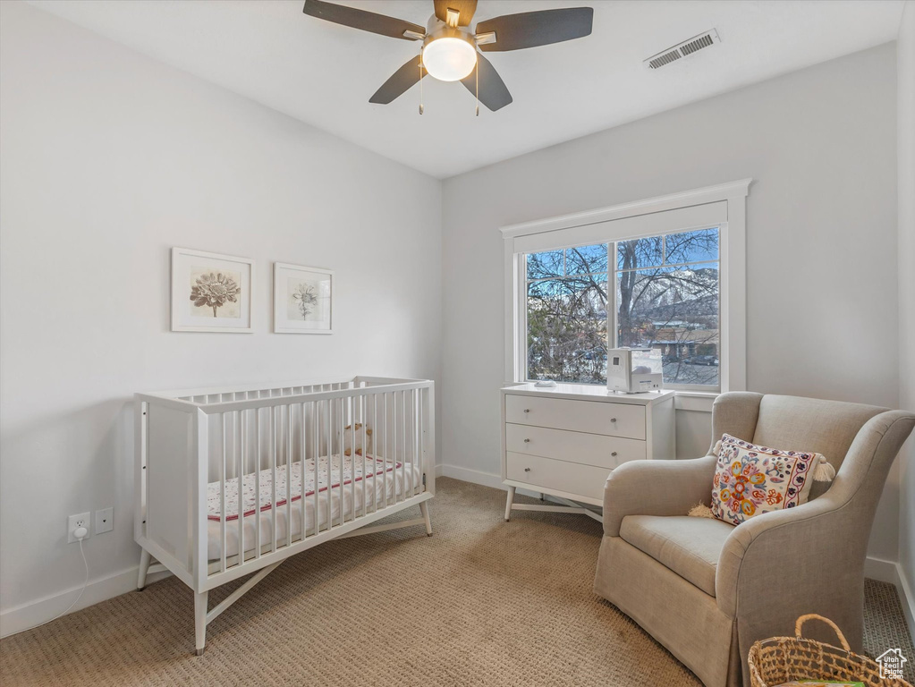 Bedroom with baseboards, visible vents, light colored carpet, ceiling fan, and a nursery area