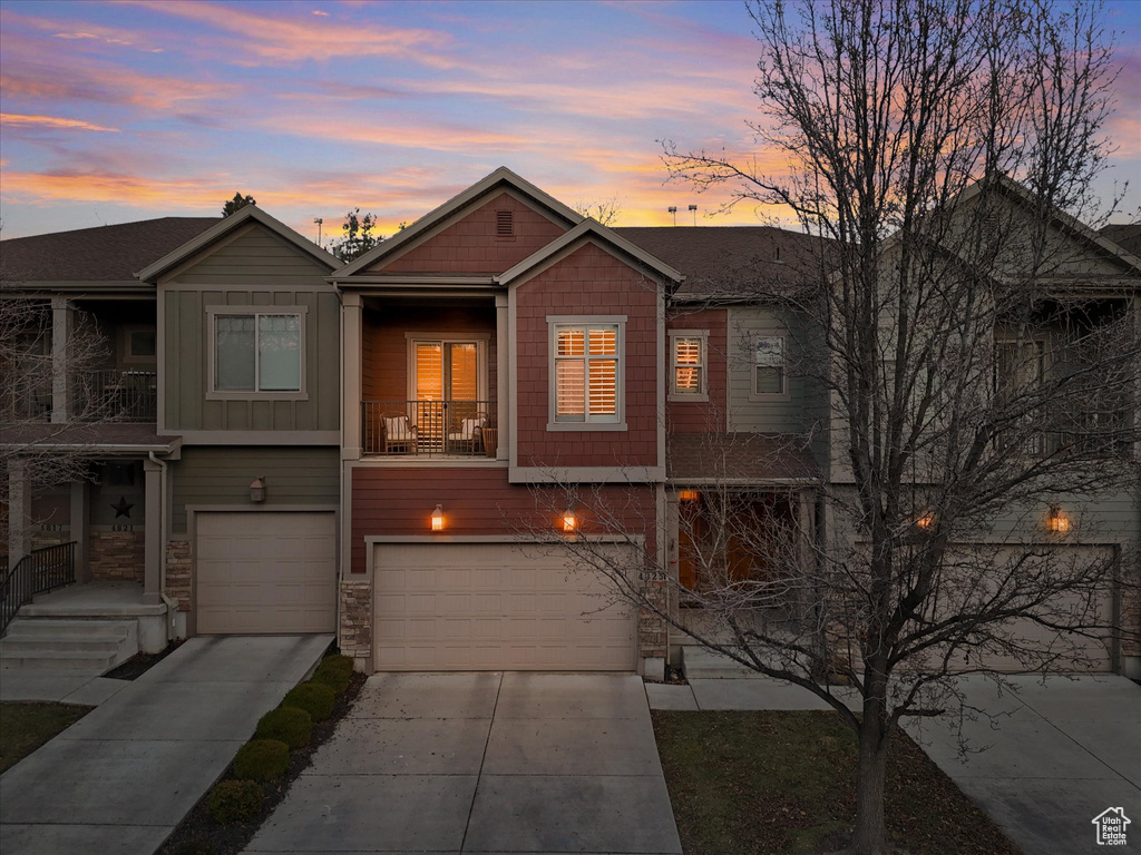 View of front of property featuring a garage, concrete driveway, a balcony, stone siding, and board and batten siding