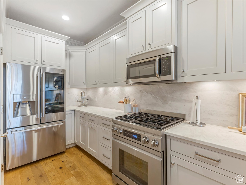 Kitchen with light wood-style flooring, white cabinets, appliances with stainless steel finishes, decorative backsplash, and light stone countertops