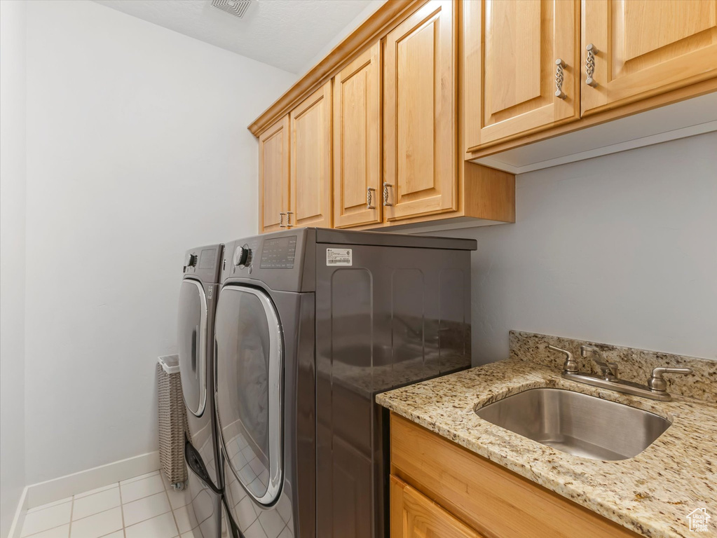 Washroom featuring light tile patterned floors, a sink, baseboards, washer and dryer, and cabinet space