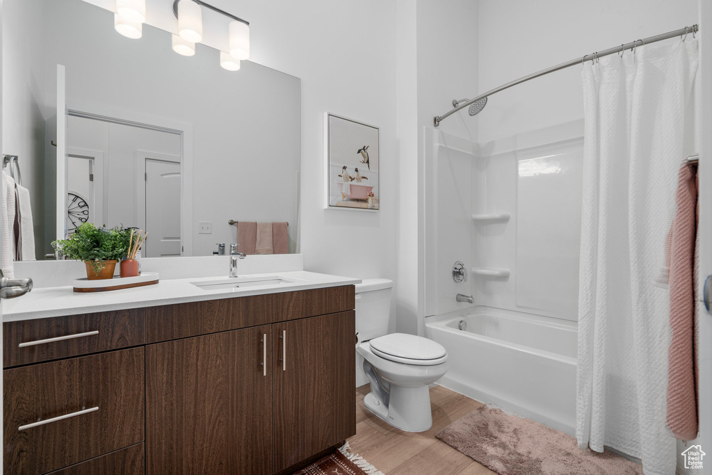 Full bath with toilet, shower / bath combo with shower curtain, wood finished floors, and vanity