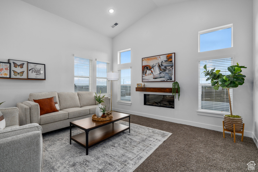 Carpeted living room with high vaulted ceiling, recessed lighting, visible vents, baseboards, and a glass covered fireplace