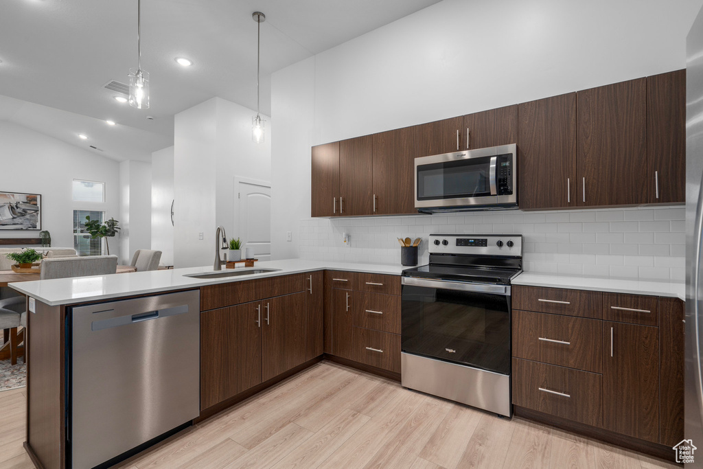 Kitchen featuring appliances with stainless steel finishes, a peninsula, light countertops, light wood-style floors, and a sink