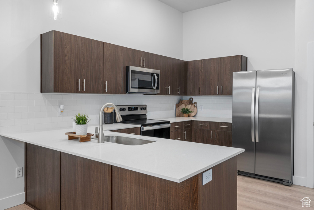 Kitchen with light countertops, appliances with stainless steel finishes, a sink, dark brown cabinets, and a peninsula