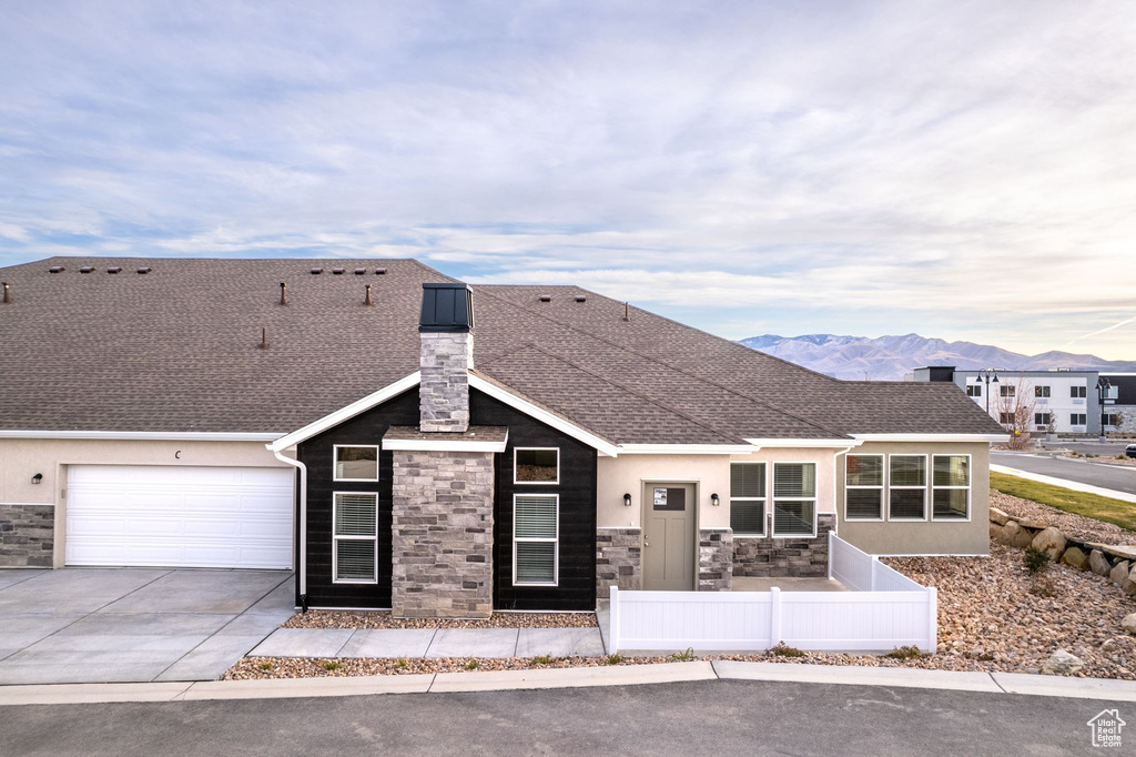 View of front of property featuring fence, concrete driveway, stone siding, stucco siding, and a chimney