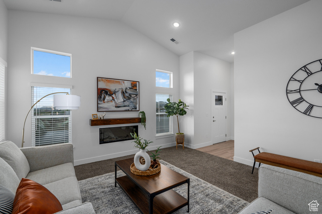 Carpeted living area featuring high vaulted ceiling, a glass covered fireplace, visible vents, and baseboards