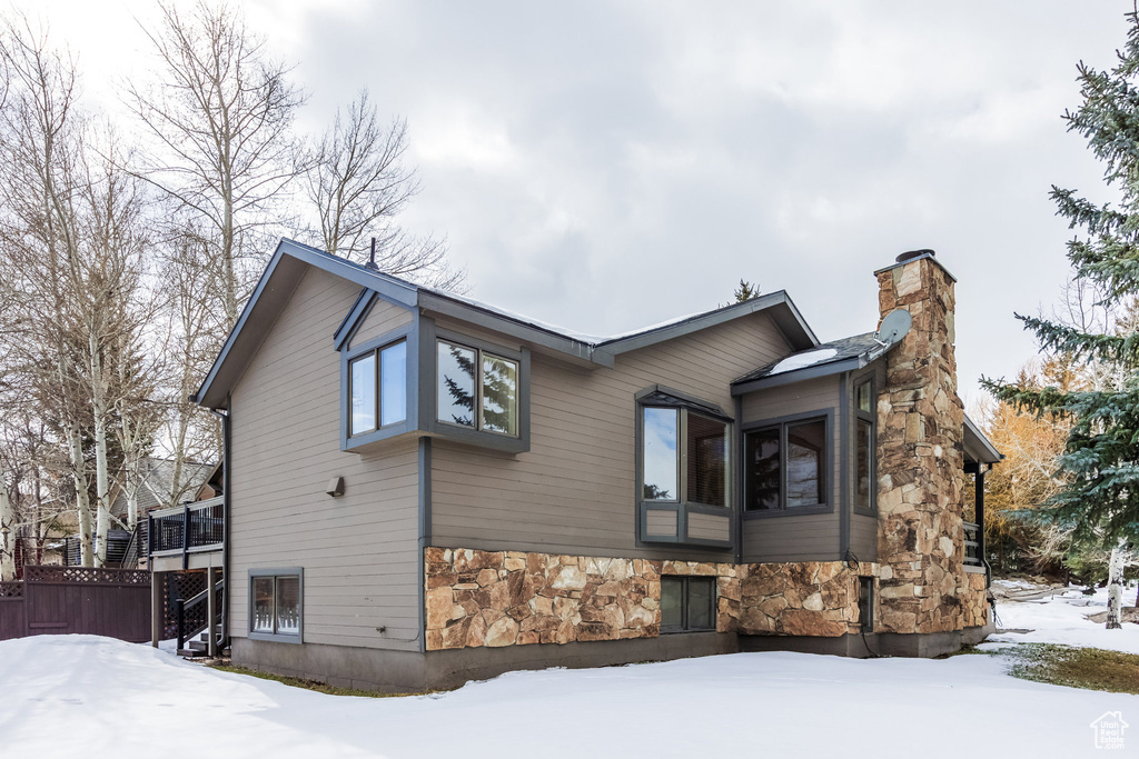 View of snowy exterior with fence, a chimney, and stone siding