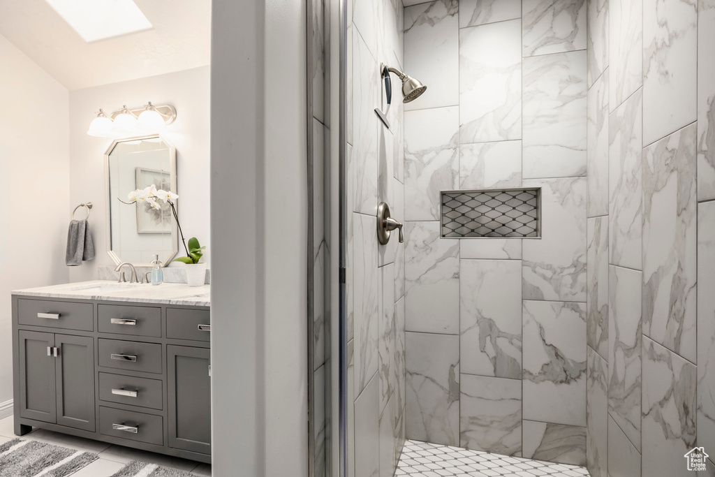 Full bath with vanity, a tile shower, and a skylight