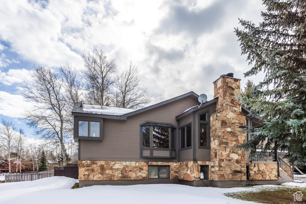 View of snowy exterior featuring a chimney, fence, and stone siding
