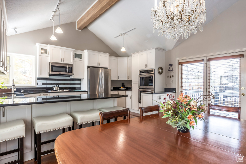 Dining area with an inviting chandelier, beam ceiling, dark wood-style floors, and high vaulted ceiling