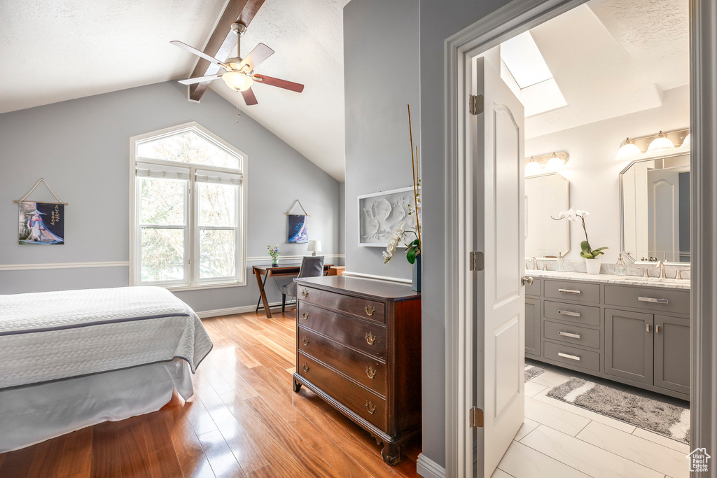 Bedroom featuring a sink, a ceiling fan, ensuite bathroom, light wood-type flooring, and lofted ceiling with skylight