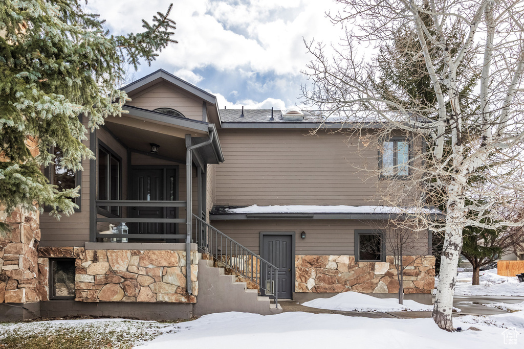 Snow covered rear of property with stairs and stone siding