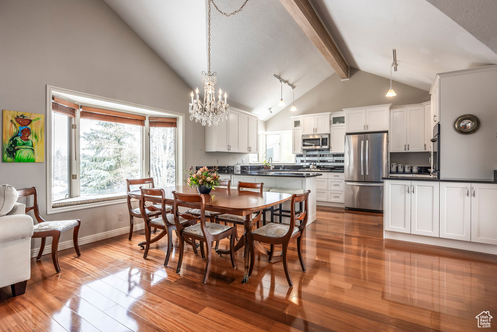 Dining area with wood finished floors, beamed ceiling, baseboards, high vaulted ceiling, and a chandelier