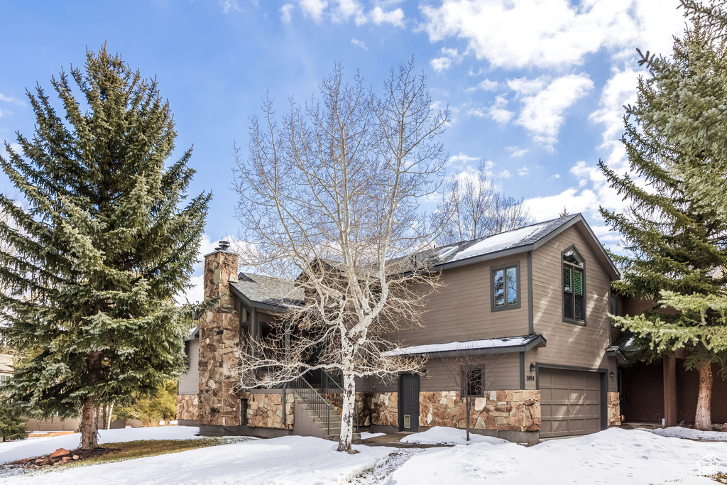 View of front of home with a chimney, stairs, stone siding, and a garage