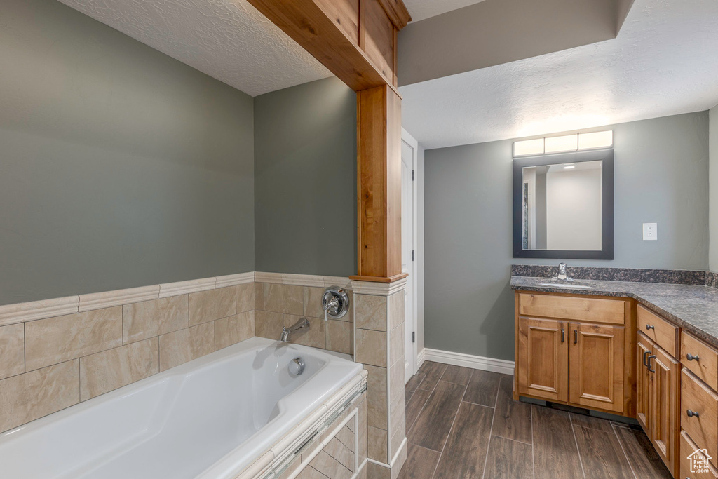 Bathroom featuring a garden tub, a textured ceiling, wood finished floors, vanity, and baseboards