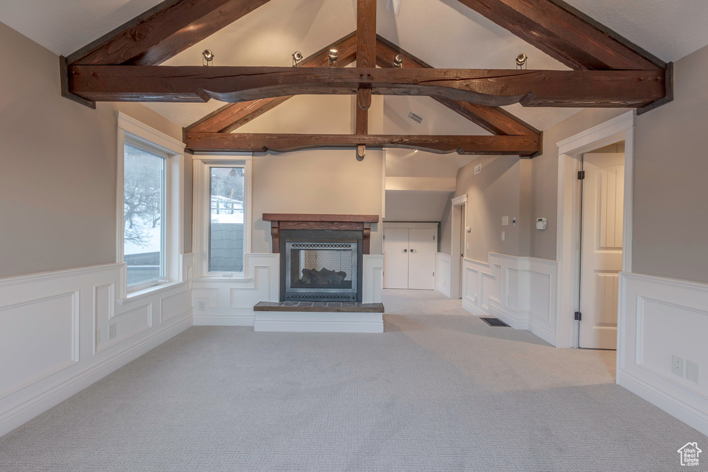 Unfurnished living room with wainscoting, vaulted ceiling with beams, carpet, and a decorative wall
