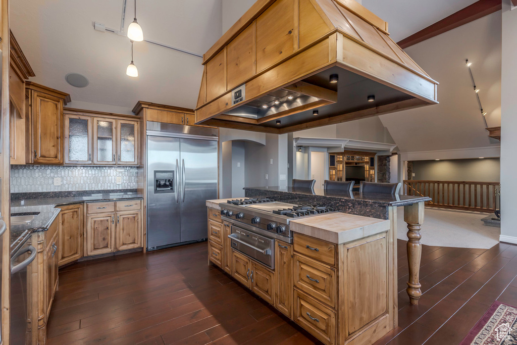 Kitchen featuring dark wood-style flooring, stainless steel appliances, custom range hood, a kitchen bar, and a warming drawer