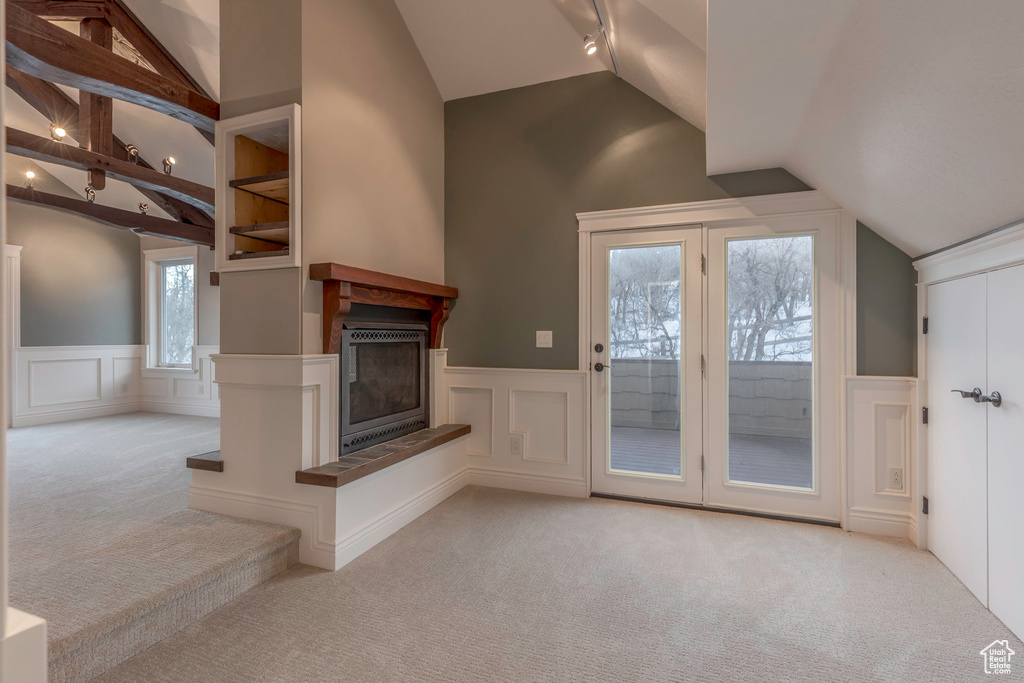 Unfurnished living room with a decorative wall, carpet floors, a wainscoted wall, a multi sided fireplace, and lofted ceiling