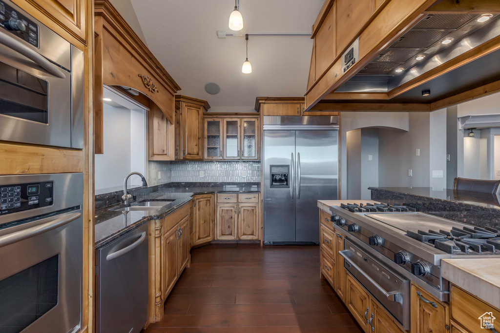 Kitchen with dark wood-style floors, arched walkways, a sink, a warming drawer, and stainless steel appliances