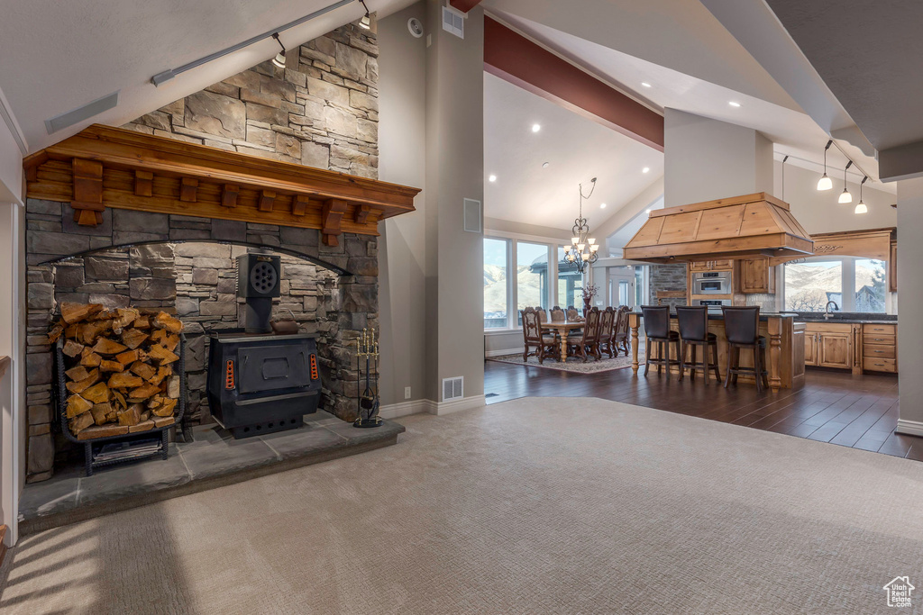 Living room with a wood stove, dark carpet, high vaulted ceiling, recessed lighting, and a chandelier