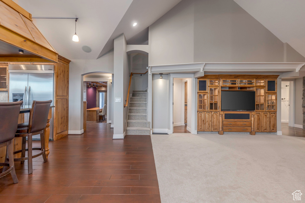 Living room with high vaulted ceiling, arched walkways, baseboards, stairway, and wood finished floors