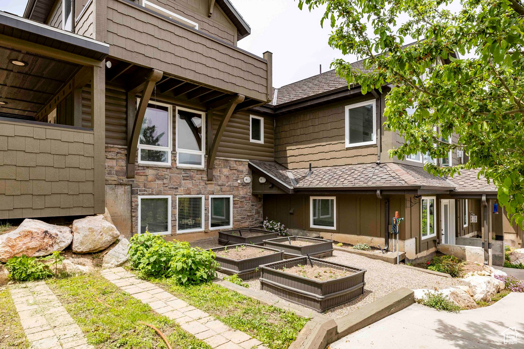 Rear view of house with a vegetable garden, stone siding, and a shingled roof