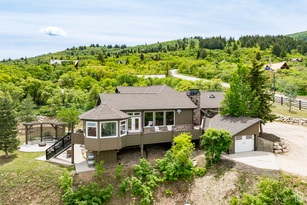 Back of property featuring a view of trees, a wooden deck, a shingled roof, and concrete driveway