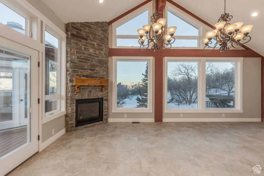 Unfurnished living room with a healthy amount of sunlight, a stone fireplace, and a notable chandelier