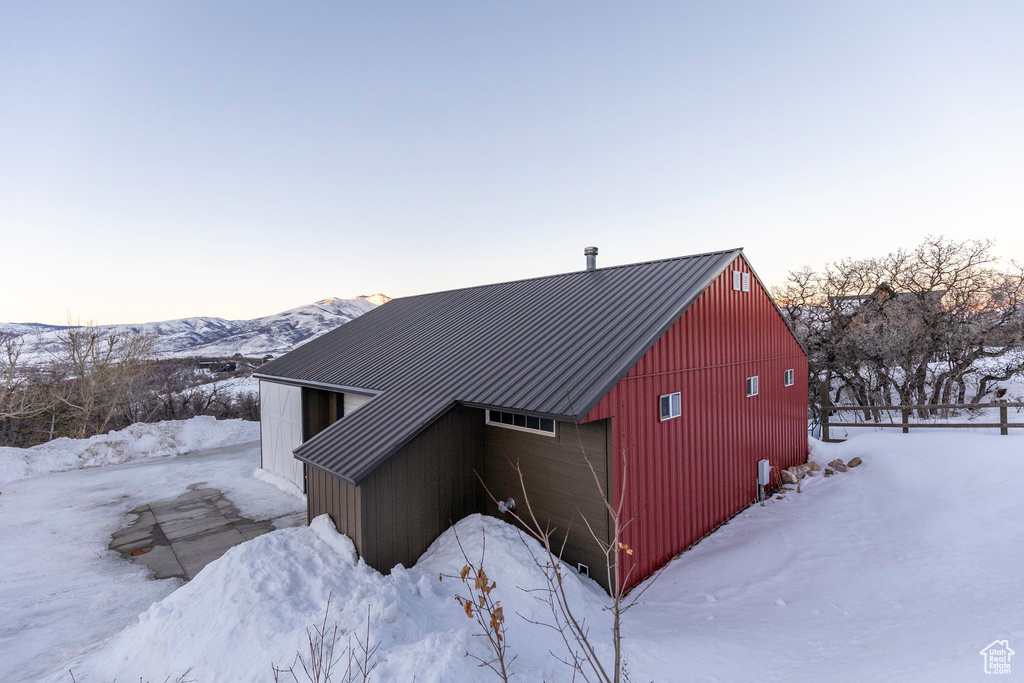 View of snowy exterior with a detached garage, an outbuilding, a mountain view, and metal roof