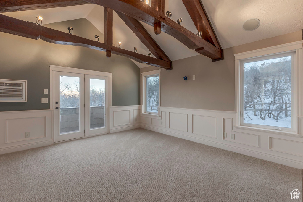 Unfurnished room with light colored carpet, beam ceiling, and a wainscoted wall