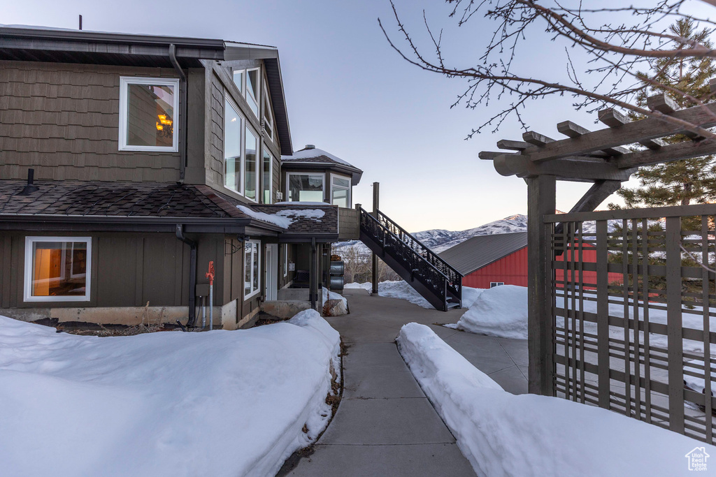 View of snowy exterior with board and batten siding, a mountain view, and stairway