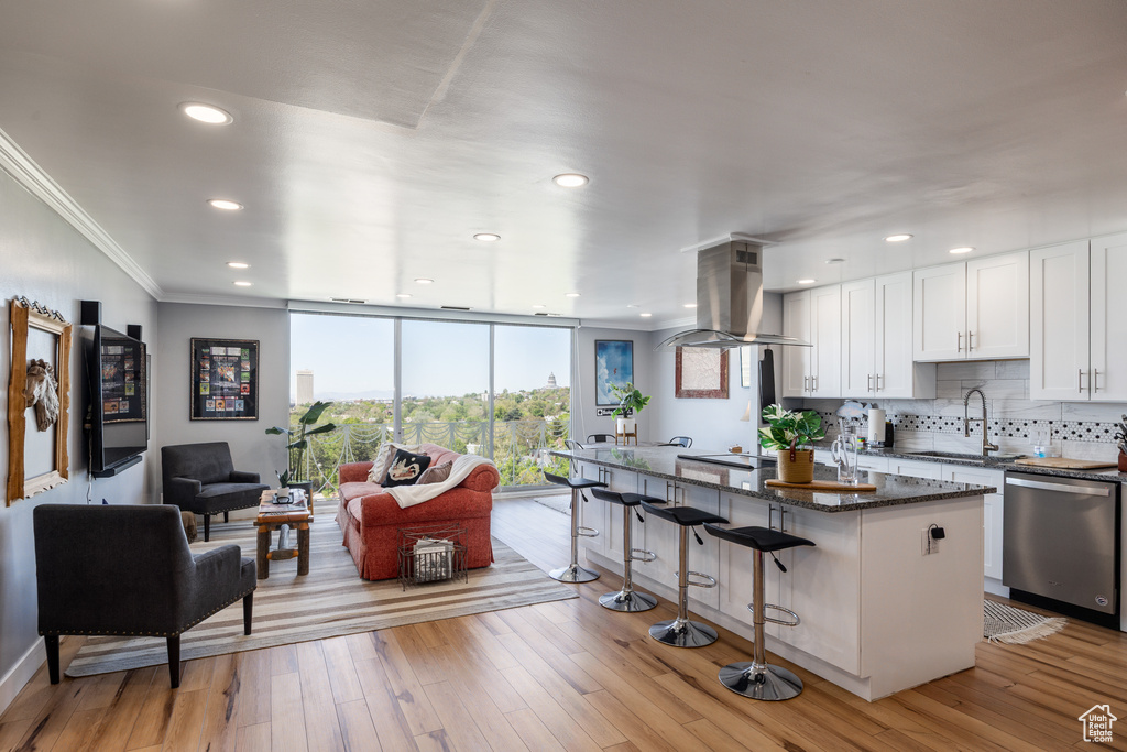 Kitchen featuring dishwasher, island exhaust hood, a sink, crown molding, and a kitchen bar