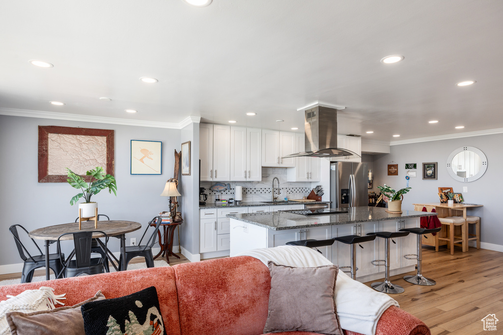 Kitchen featuring stainless steel fridge with ice dispenser, baseboards, island exhaust hood, recessed lighting, and a kitchen bar