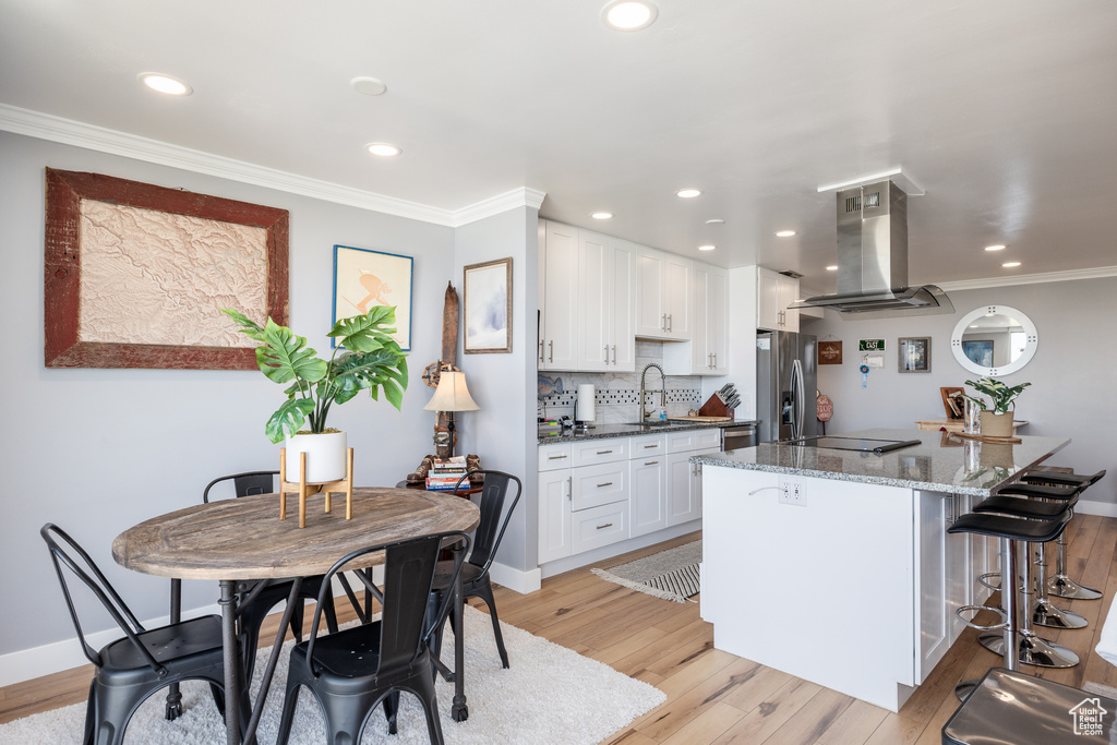 Kitchen featuring island exhaust hood, appliances with stainless steel finishes, light wood finished floors, a sink, and a kitchen breakfast bar