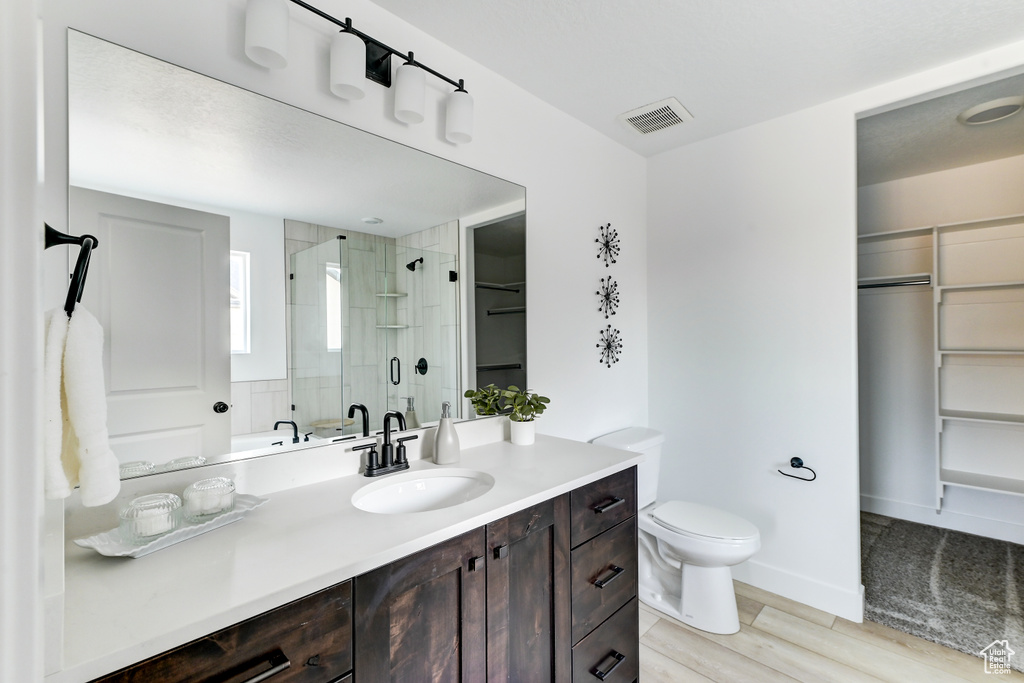 Full bath featuring toilet, wood finished floors, visible vents, a spacious closet, and a shower stall