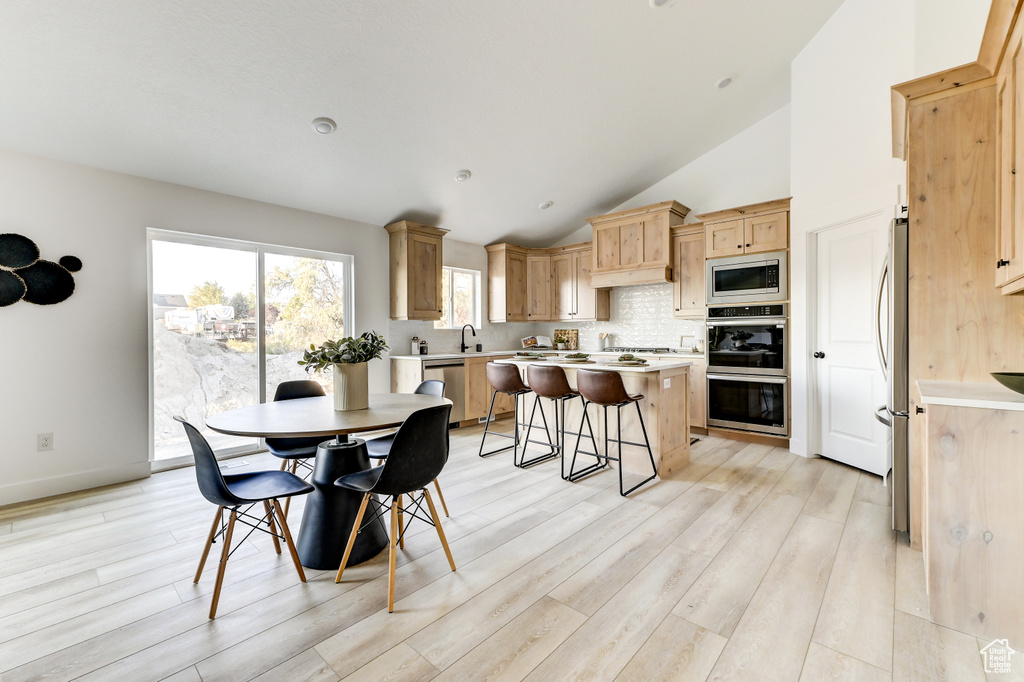 Dining space with vaulted ceiling, light wood-type flooring, and baseboards