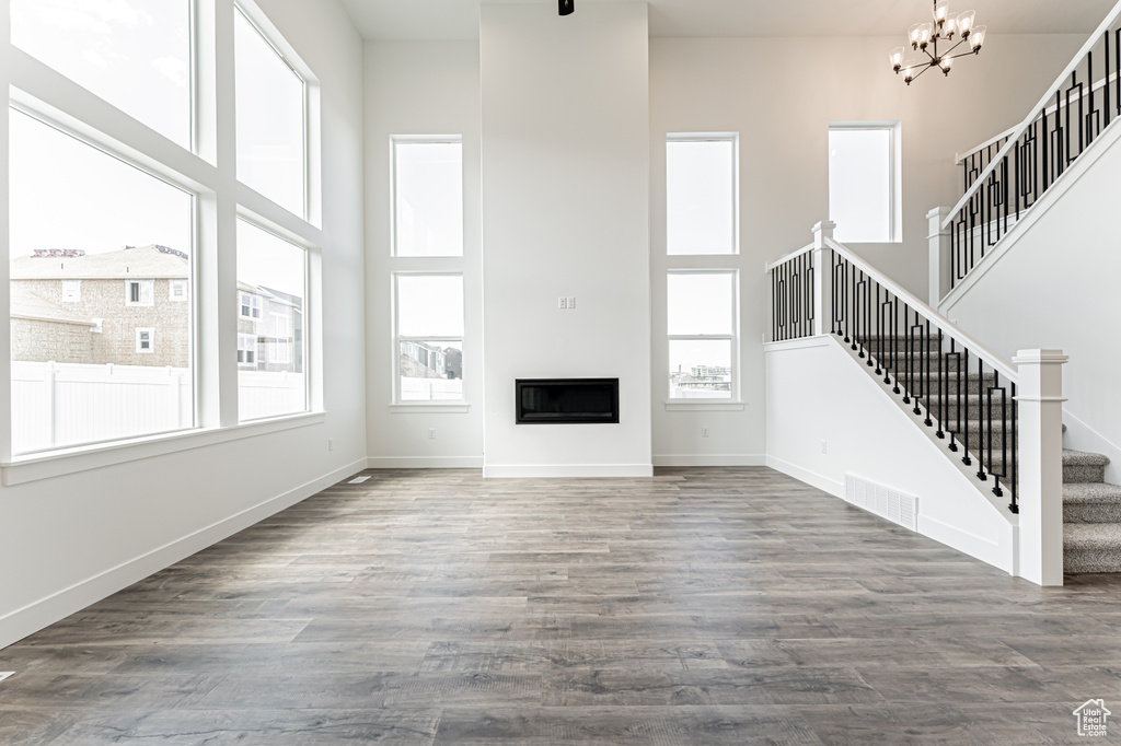 Unfurnished living room featuring a high ceiling, stairs, a chandelier, wood finished floors, and baseboards