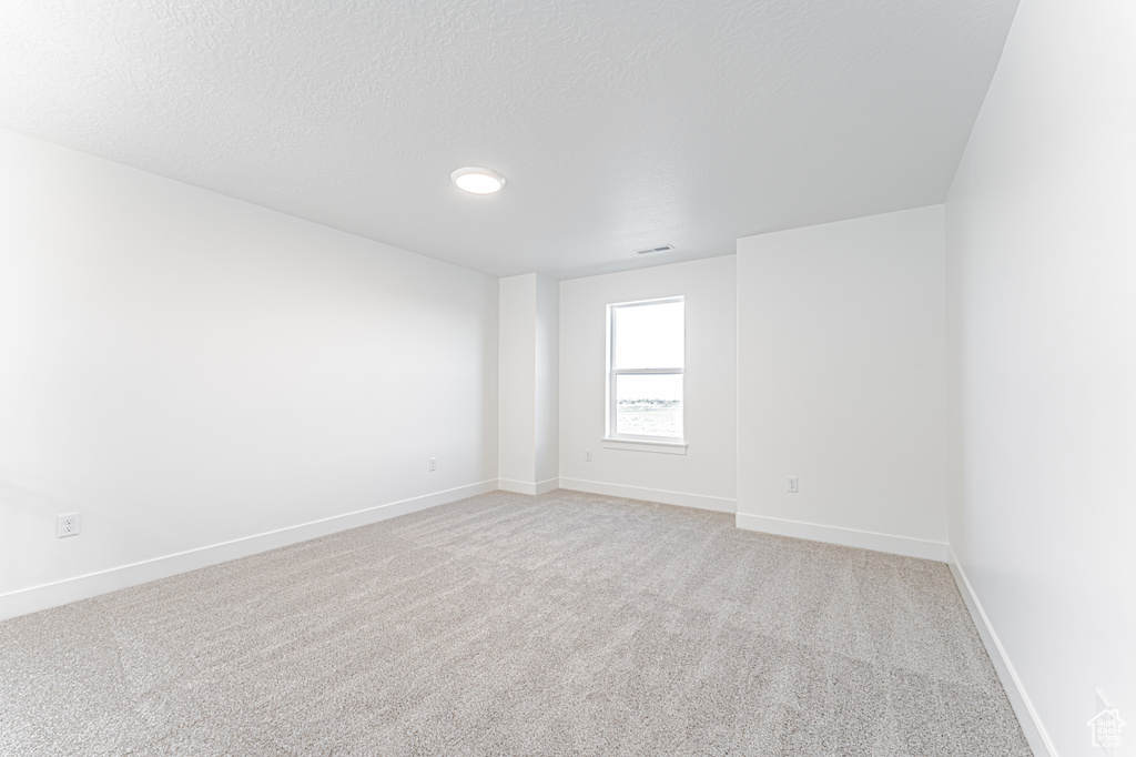 Unfurnished room featuring light colored carpet, baseboards, and a textured ceiling