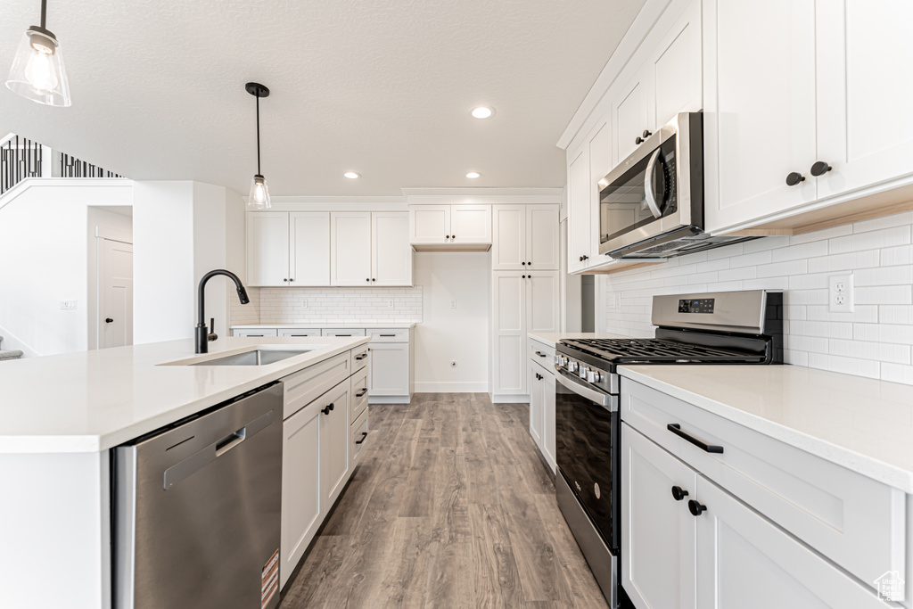 Kitchen with appliances with stainless steel finishes, a sink, light wood finished floors, backsplash, and recessed lighting