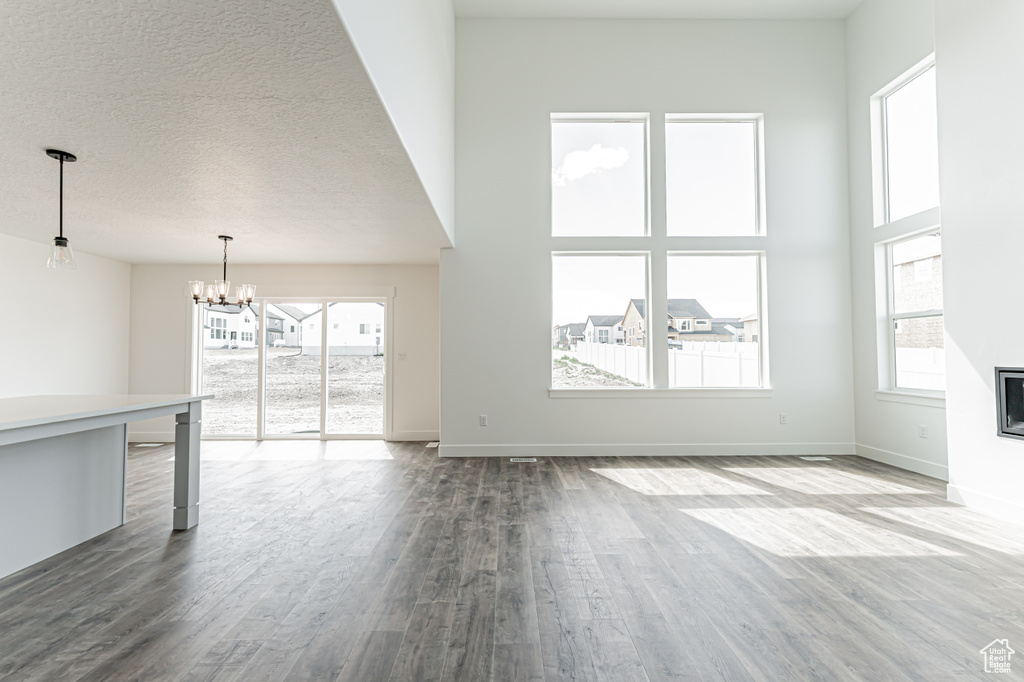 Unfurnished living room featuring dark wood-style floors, a chandelier, plenty of natural light, baseboards, and a textured ceiling