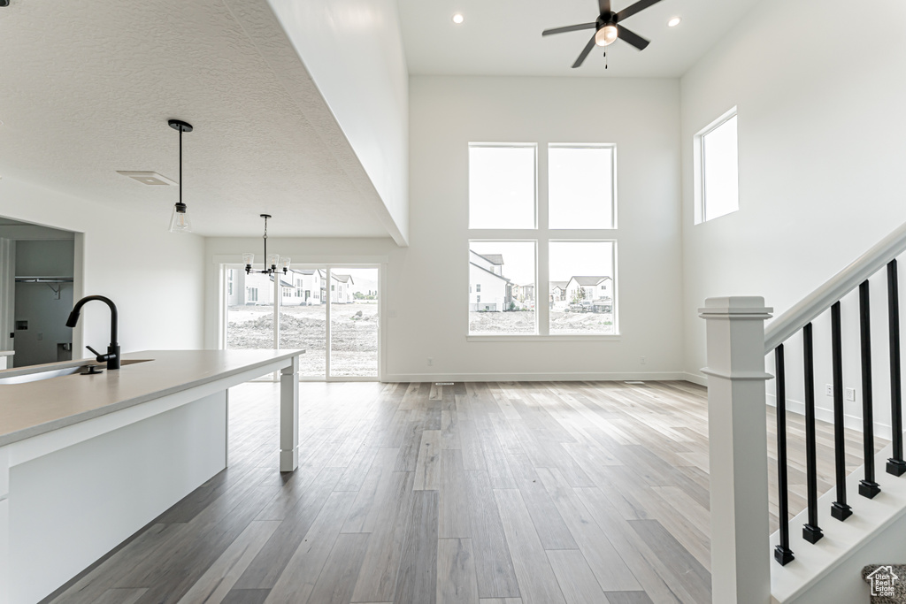 Unfurnished living room featuring a sink, ceiling fan, stairs, healthy amount of natural light, and a high ceiling