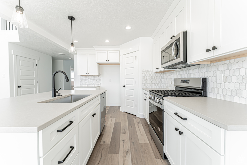 Kitchen with appliances with stainless steel finishes, a sink, light wood finished floors, recessed lighting, and tasteful backsplash